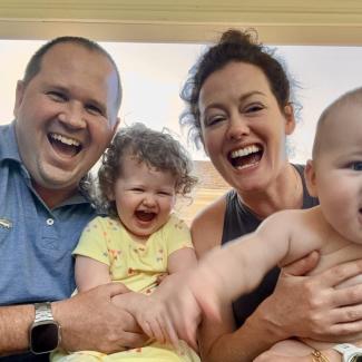 two parents - a man and a woman - hold two babies up for the camera. One baby looks happy about this, one does not.
